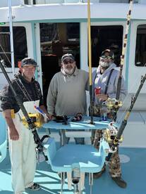 Three anglers posing inside the boat's helm area, showcasing fishing gear and a well-equipped setup for a day on the water.