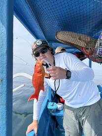 A young angler proudly displaying a vibrant Red Snapper while fishing from a boat, showcasing the excitement of a successful catch.