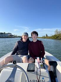 A father and son enjoying a day on a small boat, surrounded by a scenic waterway, perfect for fishing adventures.