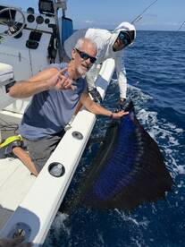 Angler celebrating a successful catch of a large Sailfish while fishing offshore, showcasing the vibrant colors of the fish against the blue ocean backdrop.