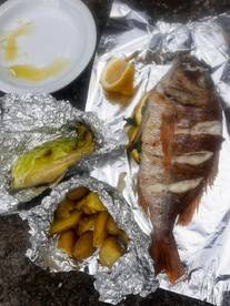 A freshly prepared meal featuring a whole fish, potatoes, and lettuce, showcasing a culinary experience after a fishing trip.