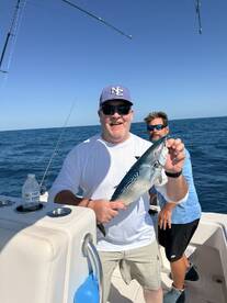 Angler proudly displaying a caught fish while on a fishing charter in open waters, with another person visible in the background.