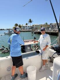 Two anglers preparing freshly caught fish on a boat in a sunny coastal environment, with pelicans nearby.