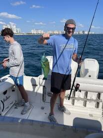 A proud angler displaying a vibrant Mahi Mahi while fishing with a companion on a boat, showcasing a beautiful coastal backdrop.