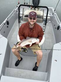 Angler proudly displaying a Redfish while seated in a boat, showcasing the excitement of a successful fishing trip.