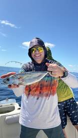 Angler proudly displaying a freshly caught fish while fishing on a sunny day, with another person in the background.