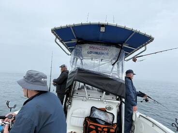 Three anglers actively fishing from a boat in overcast conditions, showcasing a typical offshore fishing experience.