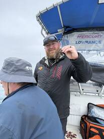 Angler proudly displaying a small fish while fishing on a boat, showcasing a relaxed group fishing experience.