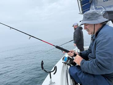 Two anglers engaged in fishing on a foggy day, showcasing the excitement of reeling in a catch from a boat.