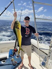 Angler proudly displaying a vibrant Mahi Mahi aboard a fishing boat in clear blue waters.