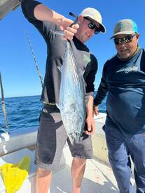 Two anglers proudly displaying a large fish on a boat during a deep-sea fishing trip.