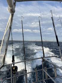 View from the side of a fishing boat with multiple rods set up, cruising through open waters under a cloudy sky.