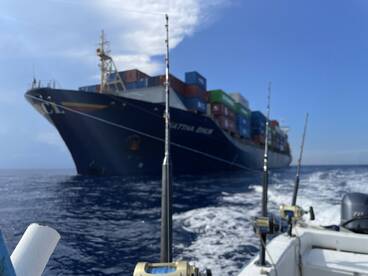 A large cargo ship, 'Matina Eagle', is seen from a fishing boat, showcasing the contrast between commercial shipping and recreational fishing in open waters.