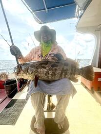 Angler proudly displaying a large Goliath Grouper while seated on a fishing boat, showcasing a successful day on the water.