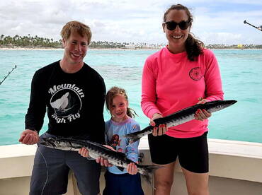 A family proudly displaying their catch of Barracuda while enjoying a fishing trip in tropical waters.