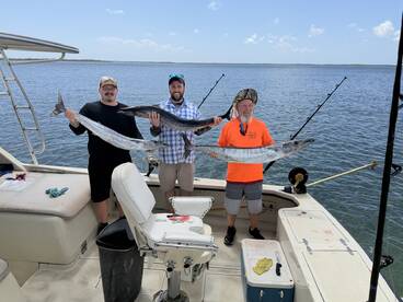 Three anglers proudly displaying their catch of Barracuda while aboard a fishing boat in a coastal waterway.