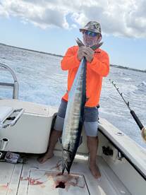 Angler proudly displaying a large Wahoo on a fishing boat, showcasing a successful offshore fishing trip.