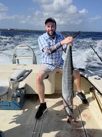 Angler proudly displaying a large Wahoo on a fishing boat, showcasing a successful offshore fishing trip.