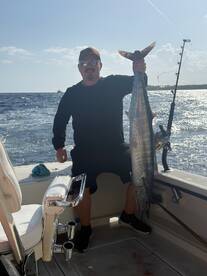 Angler proudly displaying a large Wahoo on a fishing boat during a deep-sea fishing trip.