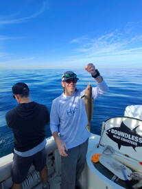 Angler proudly displaying a freshly caught fish while fishing on a charter boat in calm waters.