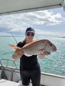 A proud angler holding a large Snapper while fishing on a boat, showcasing a successful day on the water.