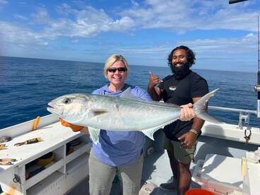 A proud angler displaying a large Amberjack while fishing on a charter boat, with a scenic ocean backdrop.