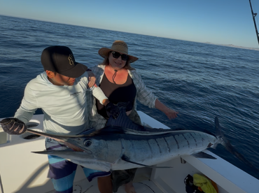 Two anglers proudly displaying a large Marlin on a fishing boat, showcasing their successful catch during a deep-sea fishing trip.