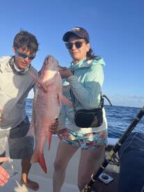 Two anglers proudly displaying a large Red Snapper while fishing offshore, showcasing a successful day on the water.