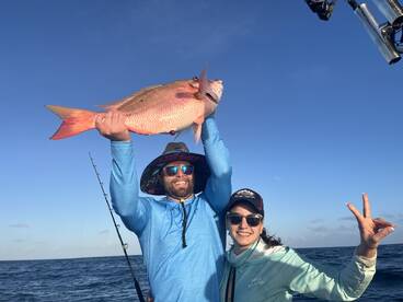Two anglers celebrating a successful catch of a vibrant Snapper while fishing offshore, showcasing the joy of a day on the water.