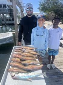 A group of three anglers, including two young boys, proudly displaying a catch of various fish, including Snapper, on a dock after a successful fishing trip.