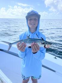 Young angler proudly holding a Spanish Mackerel while fishing offshore, showcasing a successful catch on a sunny day.