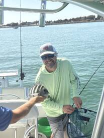 Angler smiling while holding a Sheepshead fish on a boat, showcasing a successful fishing trip.