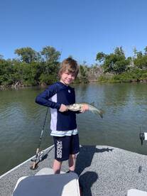 Young angler proudly holding a Snook while fishing in a scenic mangrove area.