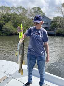 An angler proudly displaying a large Snook while fishing from a boat in a scenic waterway.