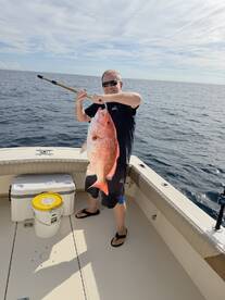 Angler proudly displaying a large Red Snapper while fishing offshore, showcasing a successful day on the water.