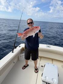 Angler proudly displaying a large Red Snapper while fishing offshore, showcasing a successful day on the water.