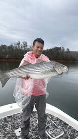 Angler proudly displaying a large Striped Bass while fishing on a lake, showcasing a successful catch.