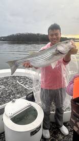 A proud angler holding a large striped bass while fishing on a boat, showcasing a successful day on the water.
