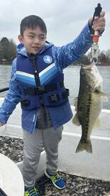 A young angler proudly displaying a large Largemouth Bass while fishing on a calm lake.