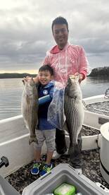 A young boy and his father proudly displaying their catch of striped bass while fishing on a lake.