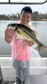 Angler proudly displaying a large Largemouth Bass while fishing on a lake, showcasing a successful catch despite the rainy weather.