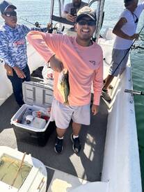 A young angler proudly displaying a caught Bass while fishing on a boat, surrounded by friends enjoying a day on the water.