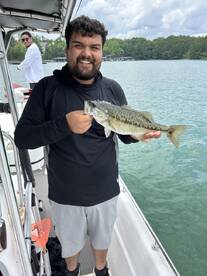 A proud angler holding a large Largemouth Bass while fishing on a lake, with a scenic backdrop of trees and water.