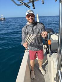 Angler proudly displaying a striped fish while aboard a fishing boat in clear blue waters.