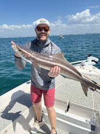 Angler proudly displaying a large Cobia while fishing on a sunny day in coastal waters.