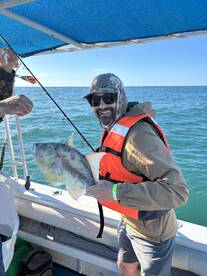 Angler proudly displaying a large fish while fishing on a boat, enjoying a sunny day on the water.