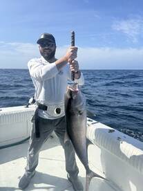 Angler proudly displaying a large Amberjack while fishing on a boat in open waters.