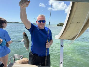 A proud angler holding a freshly caught fish while fishing on a sunny day in a coastal waterway.