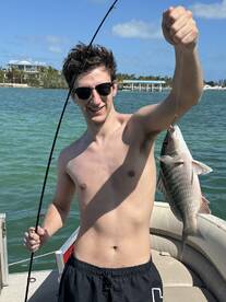 A young angler proudly displaying a freshly caught fish while fishing from a boat in a sunny coastal environment.