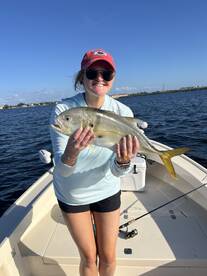 Angler proudly displaying a Yellow Jack caught while fishing from a boat in a sunny coastal environment.